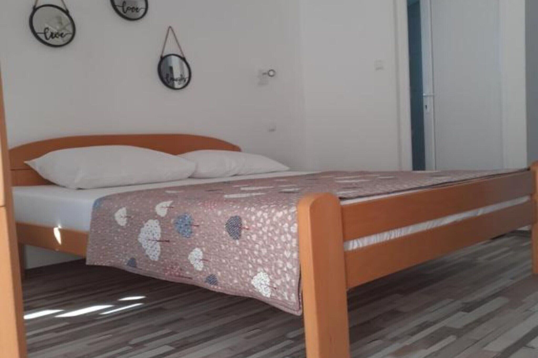 A single bed with a patterned bedspread, a wooden headboard, and a wall-mounted mirror.