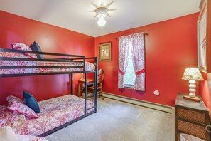 A room with red walls, a bunk bed, a desk, a chair, a lamp, and a ceiling fan. - Lakeside Retreat Near Nat’l Baseball Hall of Fame! (Cooperstown)