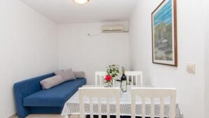 Una habitación pequeña con un sofá azul, una mesa blanca con mantel estampado y un cuadro enmarcado en la pared.