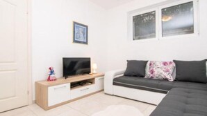 Una habitación pequeña y moderna con un sofá, un televisor sobre un soporte de madera y una ventana con persianas.