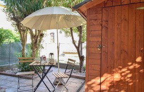 Eine Terrasse im Freien mit einem Holztisch, Stühlen, einem Sonnenschirm und einem Holzschuppen.