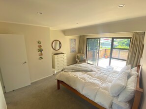 A bedroom with a bed, a dresser, a chair, and a sliding glass door leading to a balcony. - Bright 2-Bedroom in East Auckland! (Auckland)