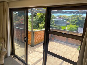 A room with a sliding glass door leading to a balcony with a view of a residential area. - Bright 2-Bedroom in East Auckland! (Auckland)
