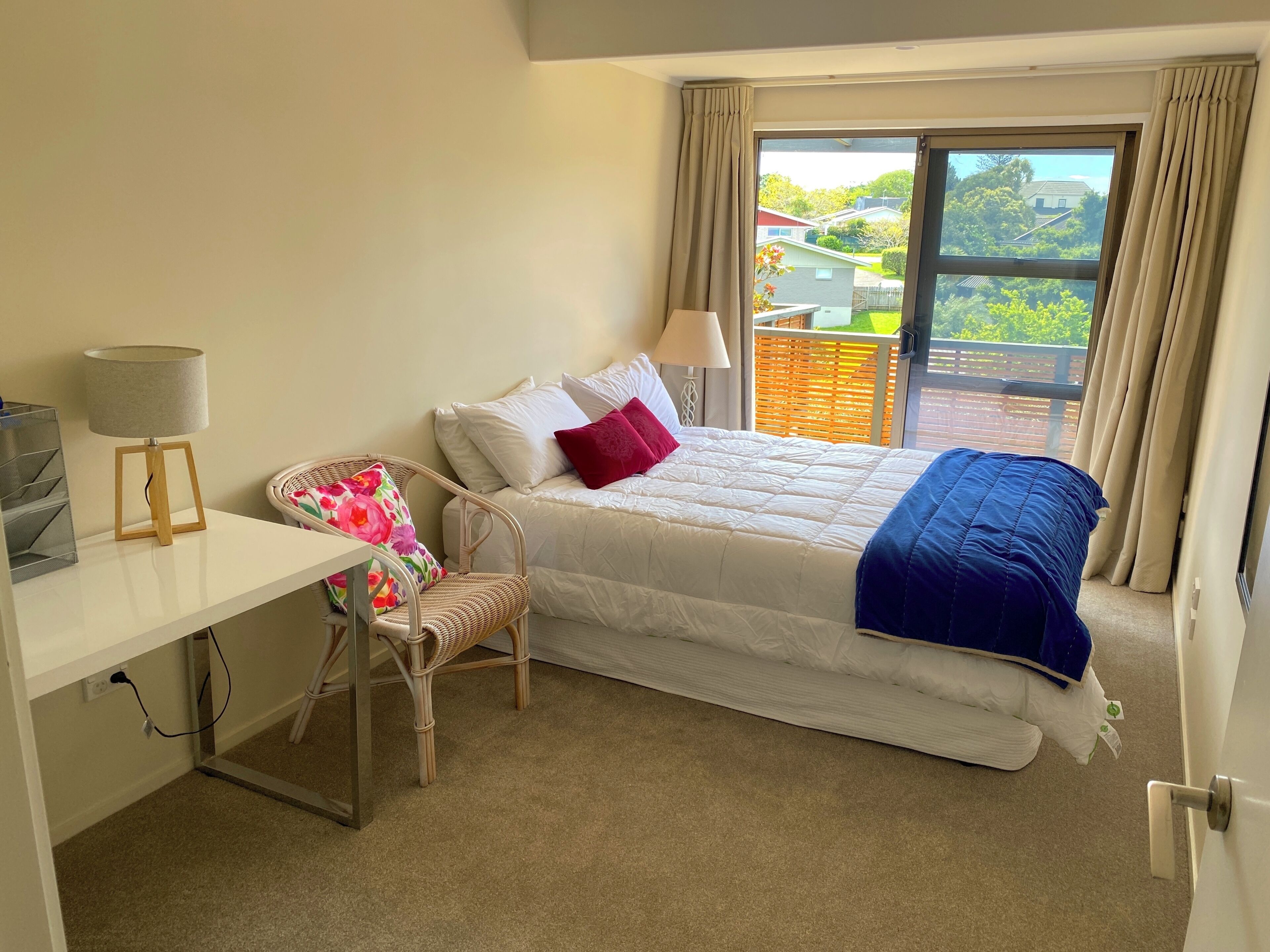 Ein Hotelzimmer mit Bett, Schreibtisch mit Lampe, Stuhl und Blick ins Freie.