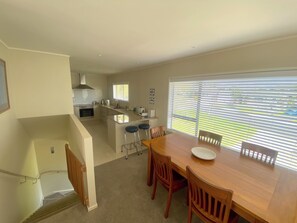 A modern kitchen with a dining area, featuring a large island, bar stools, and a view through the window. - Bright 2-Bedroom in East Auckland! (Auckland)