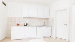 A compact kitchen with white cabinets, a kettle, and a small fruit bowl. - Apartments Savić near the Sea 7 (Herceg Novi)