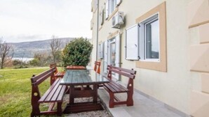 A patio with a table and benches, a building with windows, and a view of the landscape. - Apartments Savić near the Sea 7 (Herceg Novi)