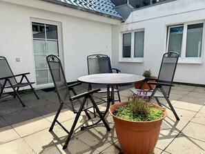 An outdoor patio with a round table and four chairs, a potted plant, and a white building with windows. - Neue Straße, Apartment 1 - Modern, centrally located 2-room upstairs apartment for (Sylt)