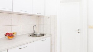 Une cuisine avec des meubles blancs, un évier en acier inoxydable et un saladier de fruits posé sur le plan de travail.
