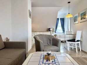 A modern living room with a sofa, armchair, and dining area with a table and chairs. - Neue Straße, Apartment 3 - Modern, centrally located 2-room upstairs apartment for (Sylt)