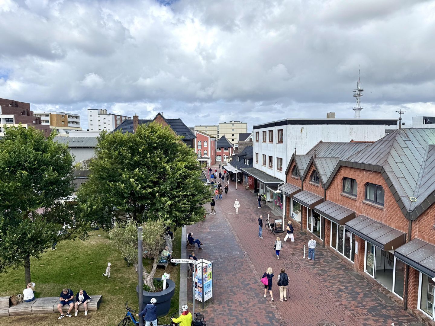 A pedestrian street with buildings, trees, and people.
