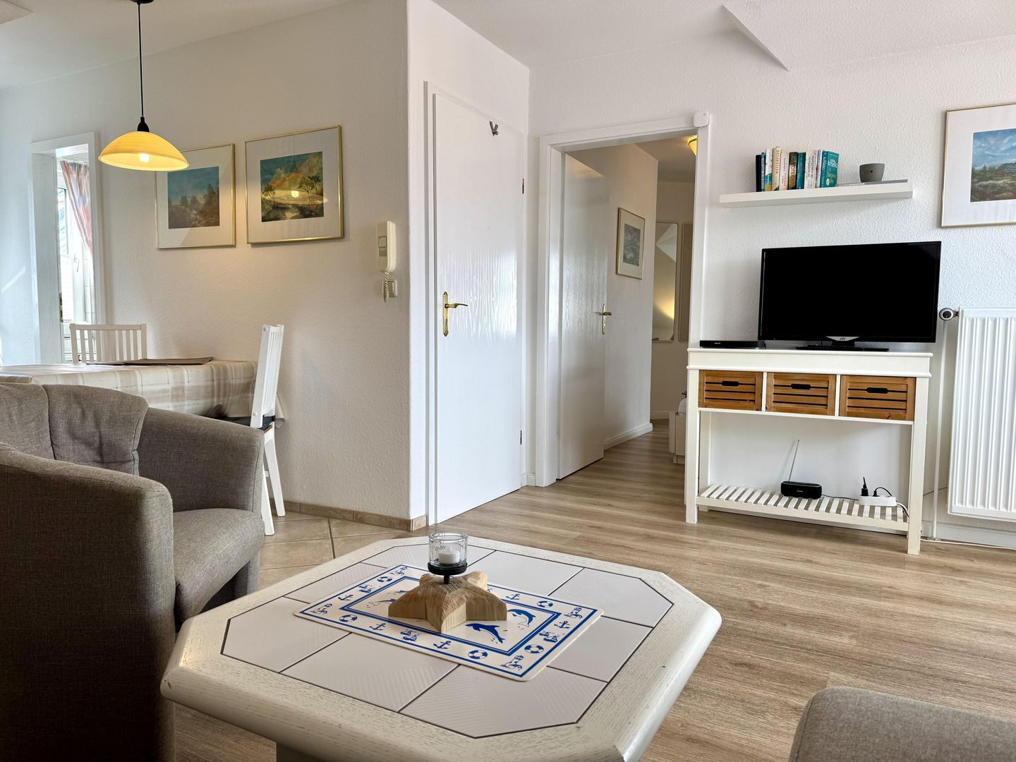 A modern living room with a sofa, a coffee table with a board game, a television on a stand, and a hallway leading to another room.