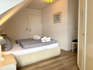A bedroom with a bed, a chair, a lamp, and a door. - Neue Straße, Apartment 3 - Modern, centrally located 2-room upstairs apartment for (Sylt)