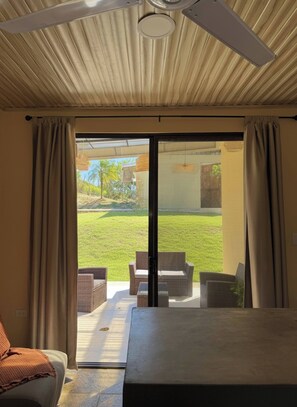 A room with a sliding glass door leading to an outdoor patio with wicker furniture and a view of a grassy area. - Niza 2 Bedroom house Hilltop view Saltwater Pool (Lajas de Matapalo)