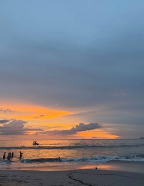 A beach scene with a sunset, calm sea, and people near the water. - Niza 2 Bedroom house Hilltop view Saltwater Pool (Lajas de Matapalo)