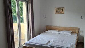Ein Schlafzimmer mit einem Bett, einem Fenster mit Vorhängen, einer Wandleuchte und einem gerahmten Bild.