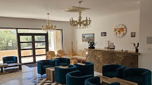 Eine Hotelhalle mit einer Rezeption, einer Sitzecke mit Sofas und Sesseln, einem Kronleuchter und einer Weltzeituhr.
