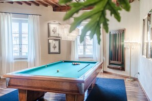Ein Billardtisch in einem Raum mit Holzböden, einem fenster mit Vorhängen und einem gerahmten Bild an der Wand.