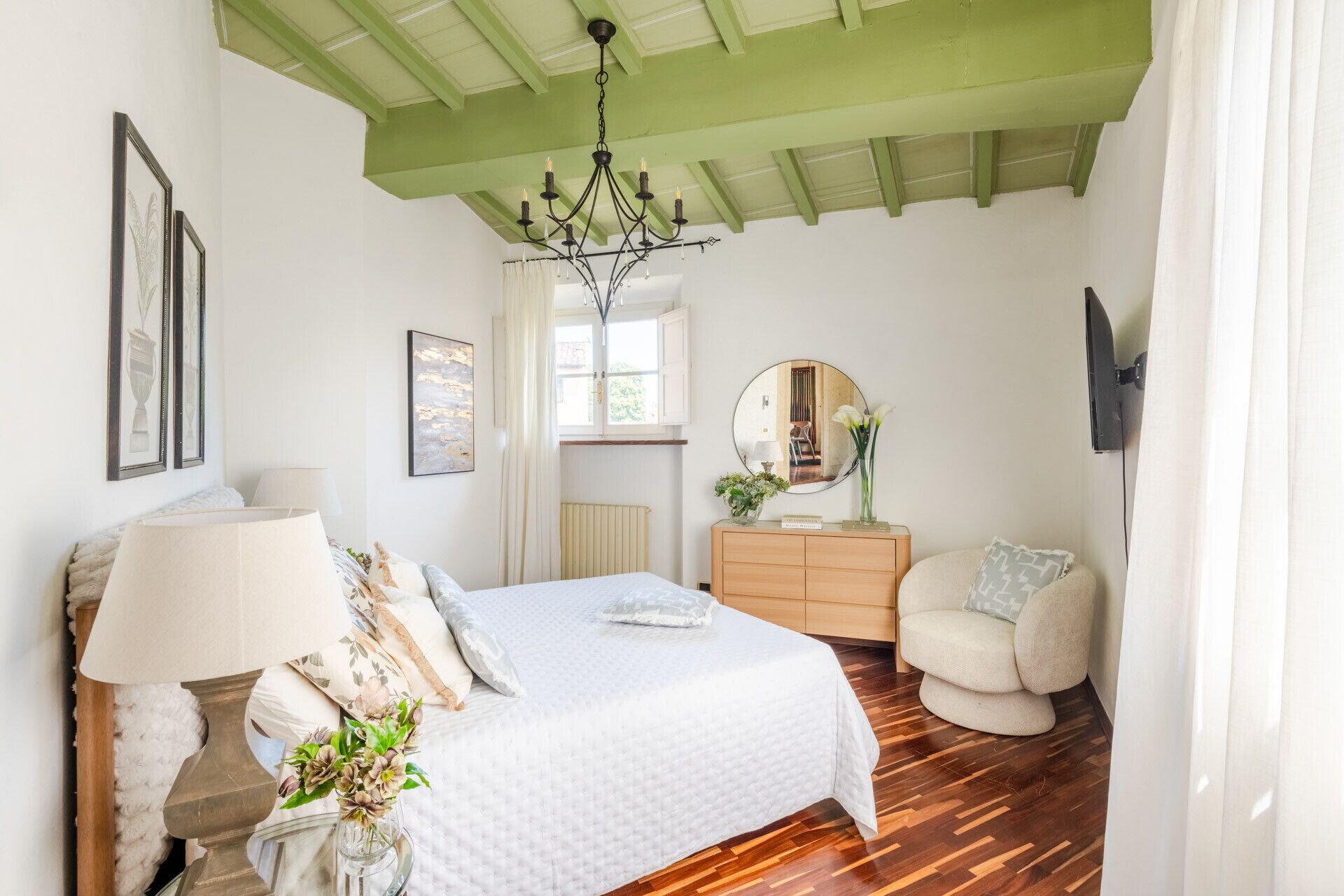 A bedroom with a bed, dresser, chair, and a chandelier.