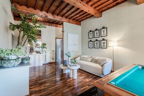Un salon avec une table de billard, un parquet, un canapé et une table basse.