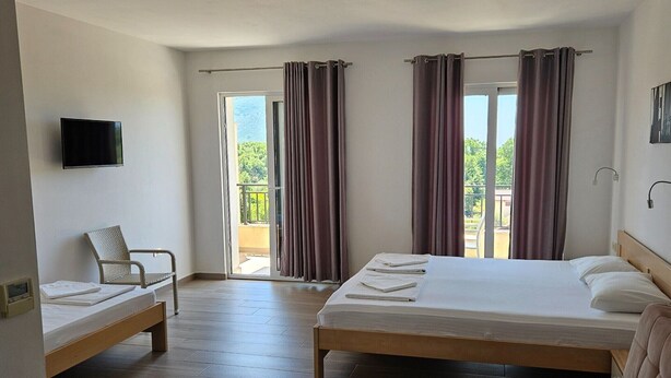 Quarto de hotel com duas camas, uma cadeira, uma TV e uma varanda com cortinas.