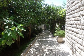 A narrow stone pathway flanked by dense foliage and a brick wall. - Guest House 4M Gregović - Double bed Lux 12 (Petrovac na Moru)