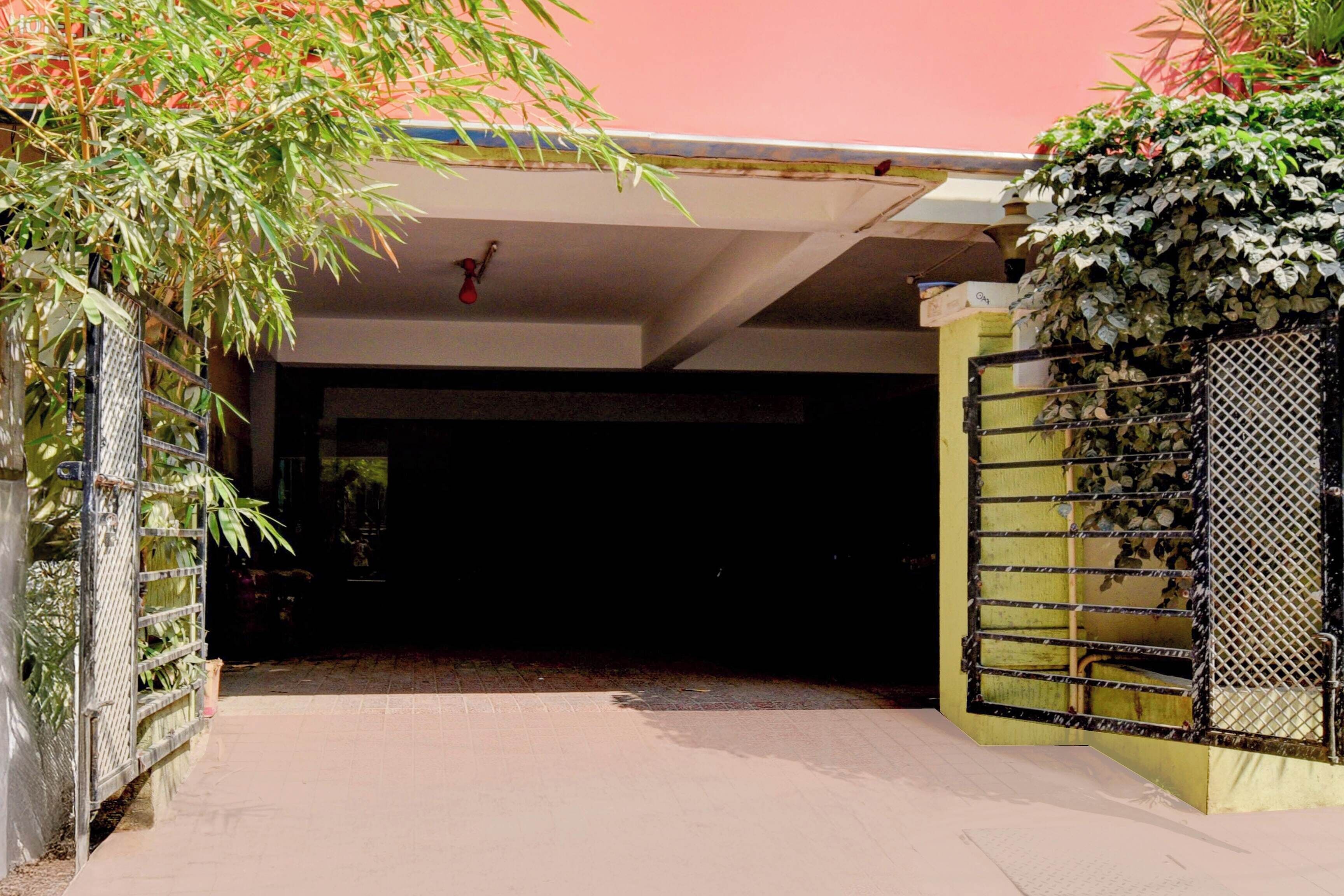 Un área de estacionamiento techada con entrada portón cerrado, cerca metálica y pared cubierta de plantas.