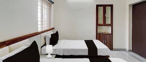 A hotel room with two beds, a wooden headboard, a bedside table with a lamp, a wardrobe, and a large window with blinds.