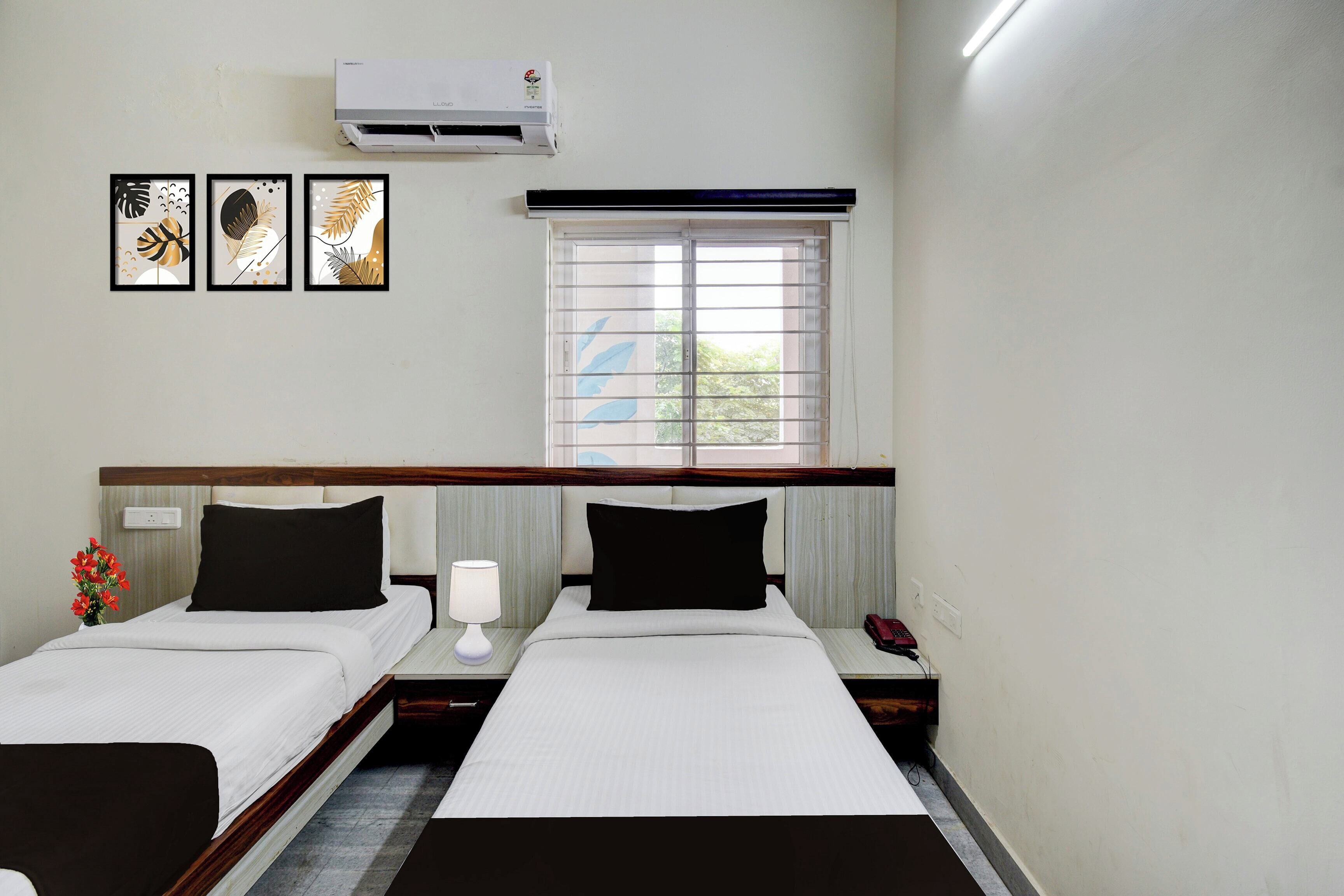 A hotel room with two beds, a window with blinds, an air conditioner, and three framed pictures on the wall.