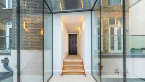 A modern interior with a glass corridor leading to a wooden staircase and a dark door. - The Colour Brief at No. 64 (London)