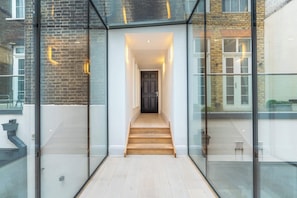 Ein modernes Interieur mit einer Glasgalerie, die zu einer Holztreppe und einer dunklen Tür führt.