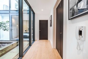 A modern hallway with glass doors leading to a balcony, a wooden floor, and a telephone on the wall. - The Colour Brief at No. 64 (London)