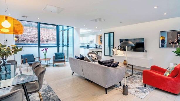 A modern living room with a grey sofa, red armchair, and a dining area with a glass table. - The Colour Brief at No. 64 (London)