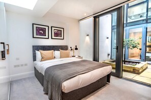 A modern bedroom with a large bed, a nightstand, a wall-mounted lamp, and two framed pictures. - The Colour Brief at No. 64 (London)