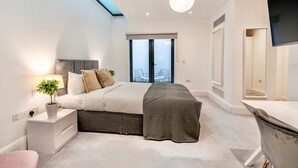 A modern bedroom with a skylight, a bed with a grey headboard, a bedside table with a lamp, and a large window with a view. - The Colour Brief at No. 64 (London)