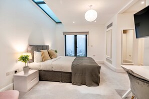 Ein modernes Schlafzimmer mit Oberlicht, einem Bett mit grauem Kopfteil, einem Nachttisch mit Lampe und einem großen Fenster mit Aussicht.