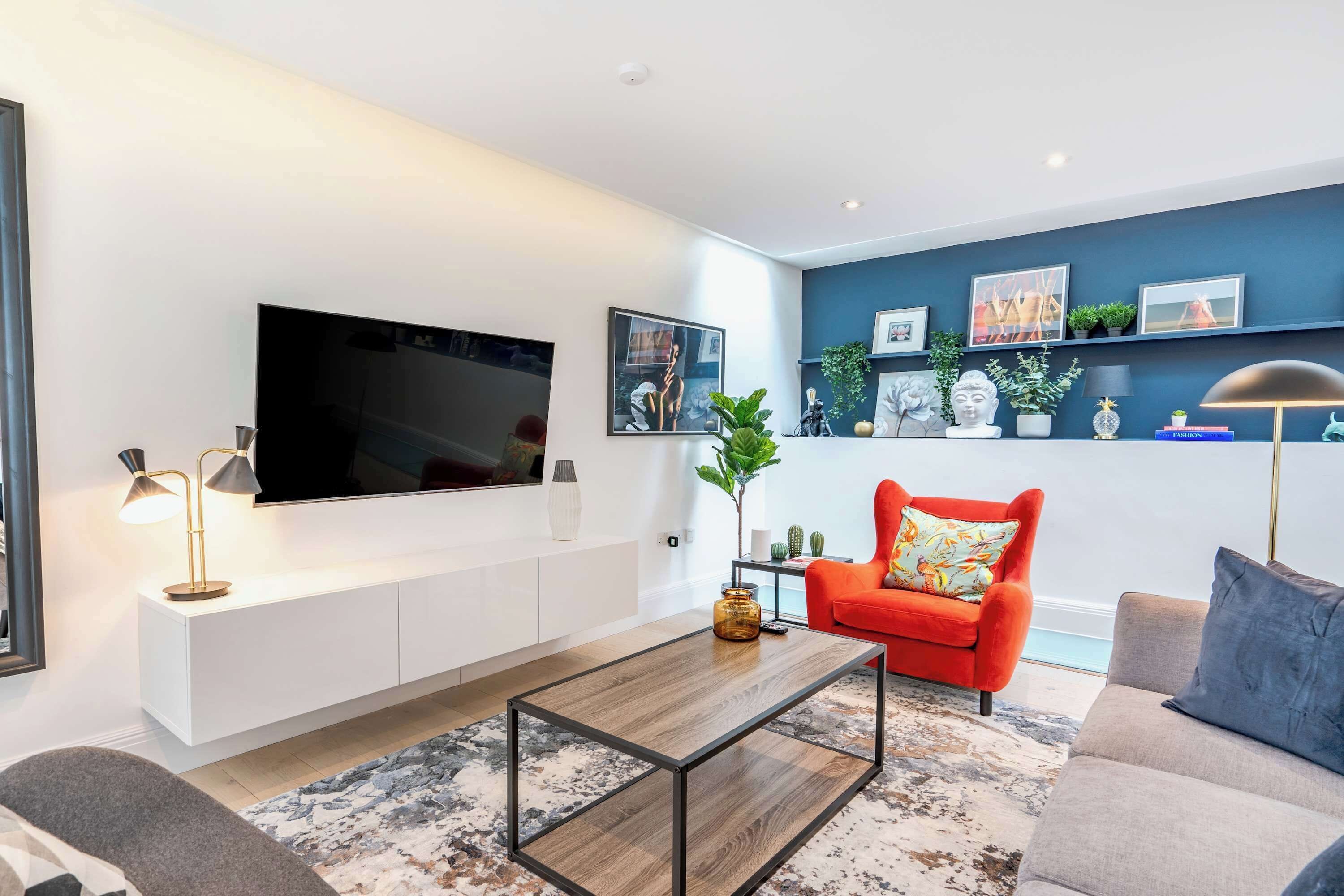 Una sala de estar moderna con un televisor de pantalla plana, un sillón rojo, un sofá gris y una mesita de centro.