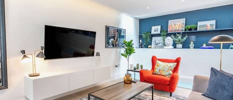 Una sala de estar moderna con un televisor de pantalla plana, un sillón rojo, un sofá gris y una mesita de centro.