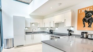 A modern kitchen with white cabinetry, a stainless steel refrigerator, a coffee maker, and a toaster. - The Colour Brief at No. 64 (London)