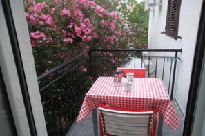 Ein kleiner Balkon mit einem karierten Tisch und Stühlen, einem Blumentopf und einem Fenster mit Rollläden.
