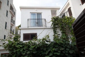 Ein weißes Gebäude mit Balkon, einem fensterartigen Öffnung mit Vorhängen und einer Tür mit Lüftung.