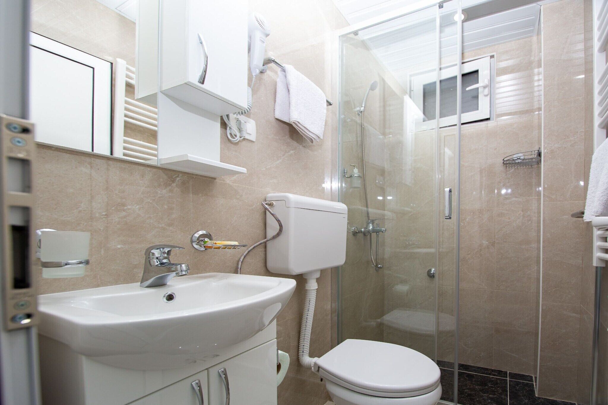 Et moderne badeværelse med vask, toilet og brusekabine med glasvægge.