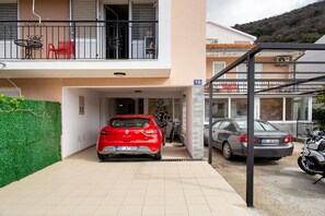 Ein Wohngebäude mit überdachtem Parkplatz, einem roten Auto und einem Motorrad.