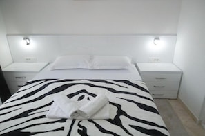 Ein Hotelzimmer mit einer bettbezogenen Zebradecke, einem ordentlich gefalteten weißen Handtuch und zwei Nachttischen mit Lampen.