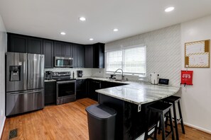 A modern kitchen with stainless steel appliances, a marble countertop, and a window with blinds. - Easy Transit to DC! Family Home w/ Fenced Yard (Springdale)