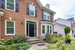 A two-story brick house with a black front door, white shutters, and a small front porch. - Easy Transit to DC! Family Home w/ Fenced Yard (Springdale)