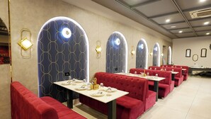 A restaurant with red upholstered booths, tables set with plates and cutlery, and decorative wall sconces. - Royalistiq (Rishikesh)
