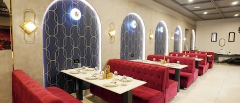 A restaurant with red upholstered booths, tables set with plates and cutlery, and decorative wall sconces.