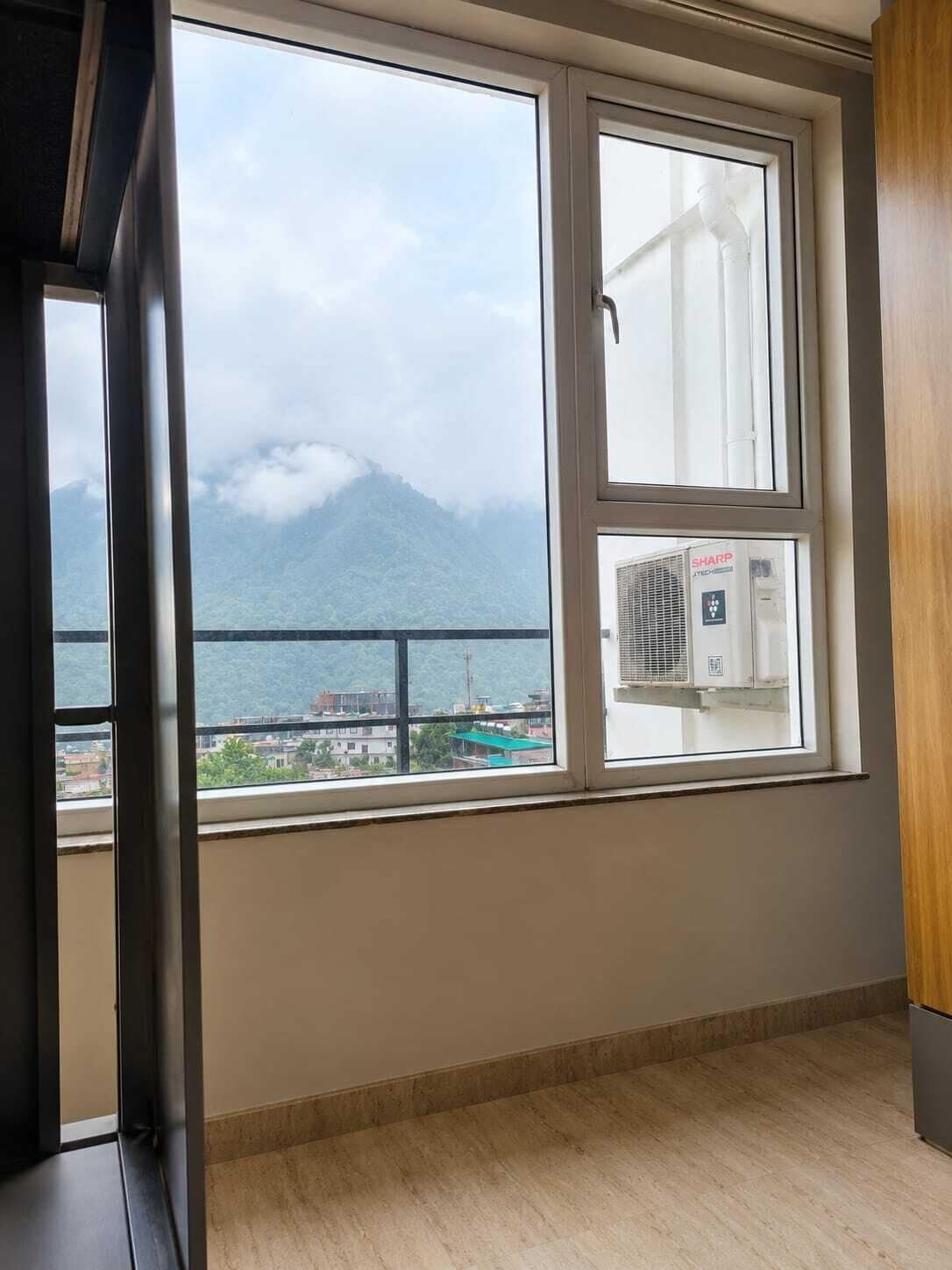 Una habitación con un ventanal grande que da a una masa de agua y una montaña, con un equipo de aire acondicionado visible en el alféizar.