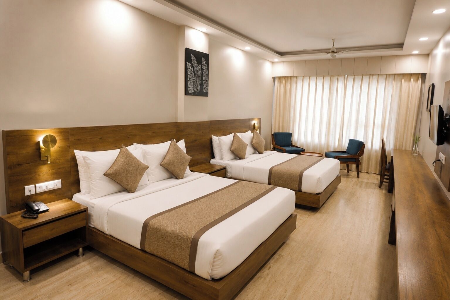 Habitación de hotel con dos camas, un escritorio, una silla y un amplio ventanal con cortinas.